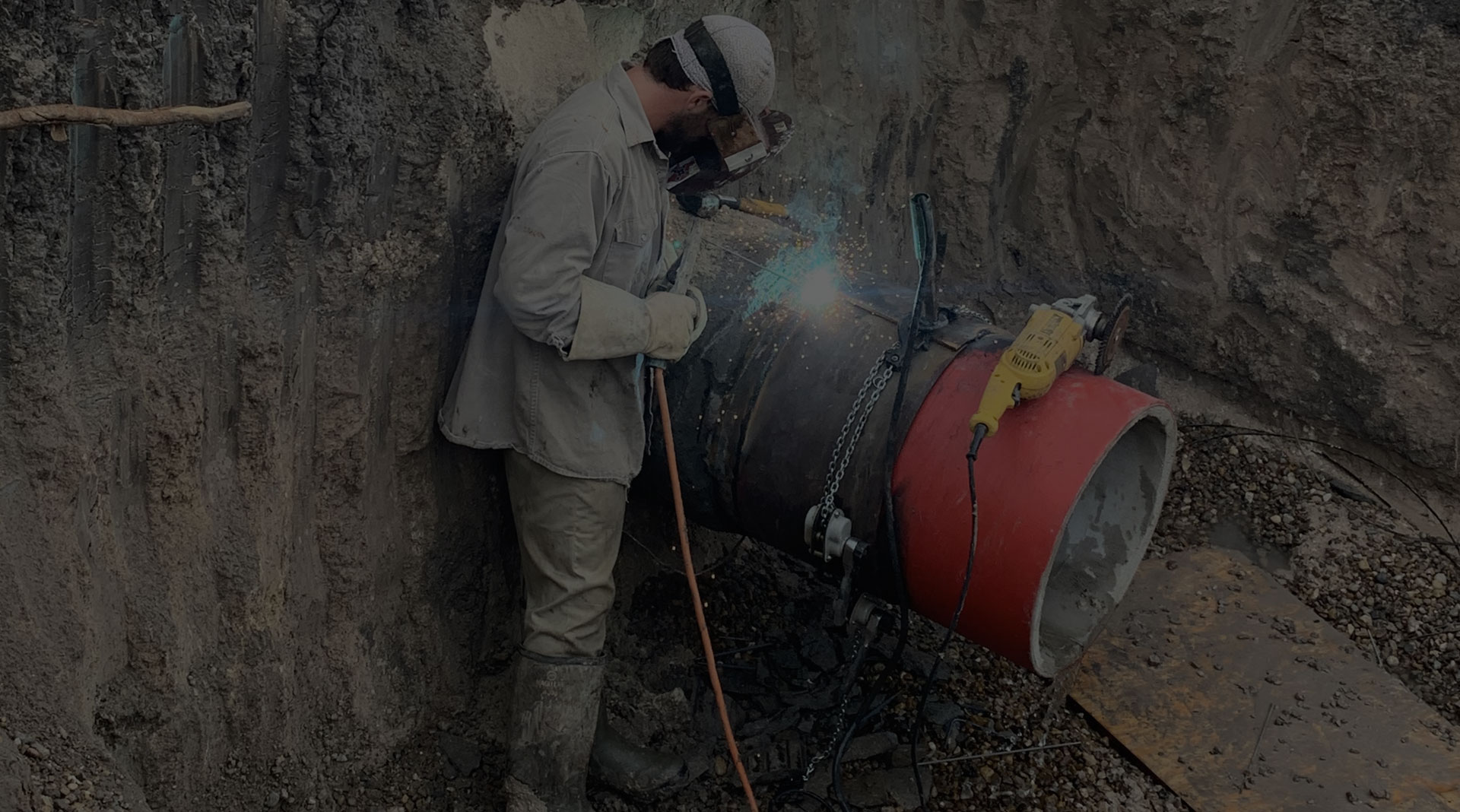 Welder performing repair work on a concrete pressure pipe in an excavation