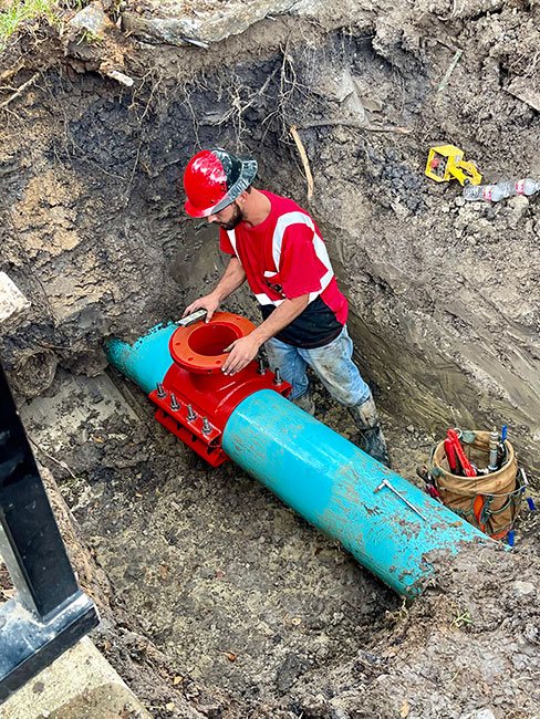 Technician in a red hard hat installing a hot tap fitting on a water main